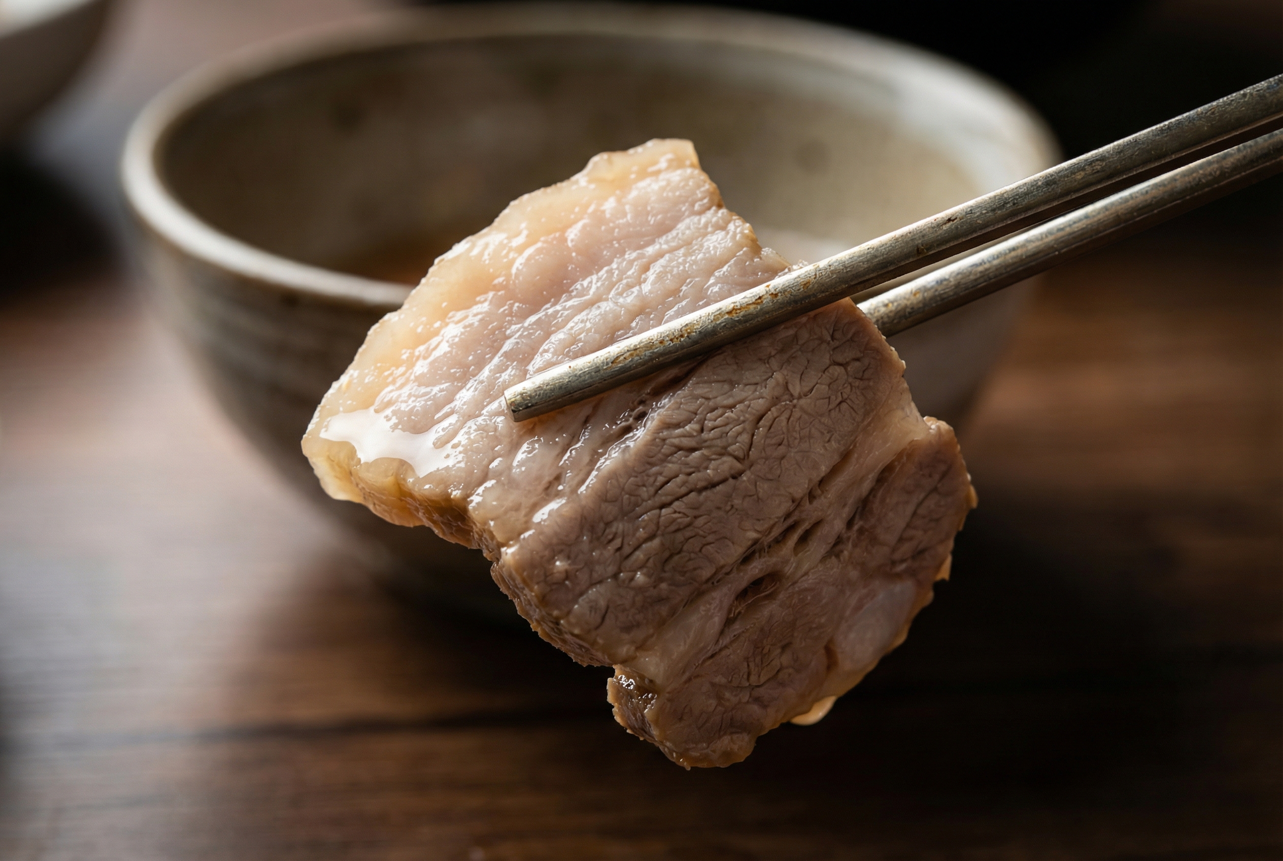 Close up macro shot of a pair of chopsticks lifting a single slice of glistening, tender pork belly